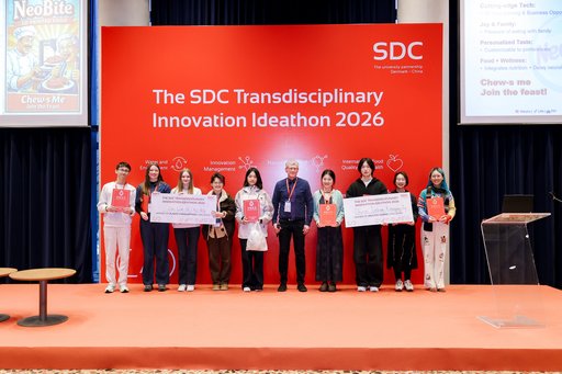 The two winning teams at SDC Ideathon 2026 stand on stage with co-organiser Morten Foss in front of a large red event backdrop in Beijing. The students hold diplomas and oversized winner’s cheques.