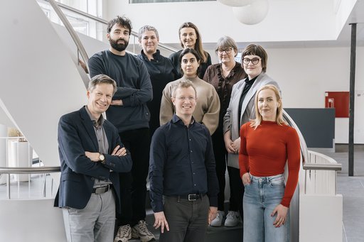 Group photo of researchers from Aarhus University and Draupnir Bio standing on a staircase indoors. The team is part of the DESYNA project, which aims to develop a new therapy for Parkinson’s disease.